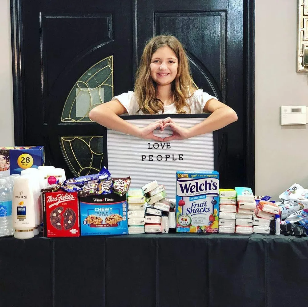 A volunteer behind a table stacked with snacks and supplies for care packages
