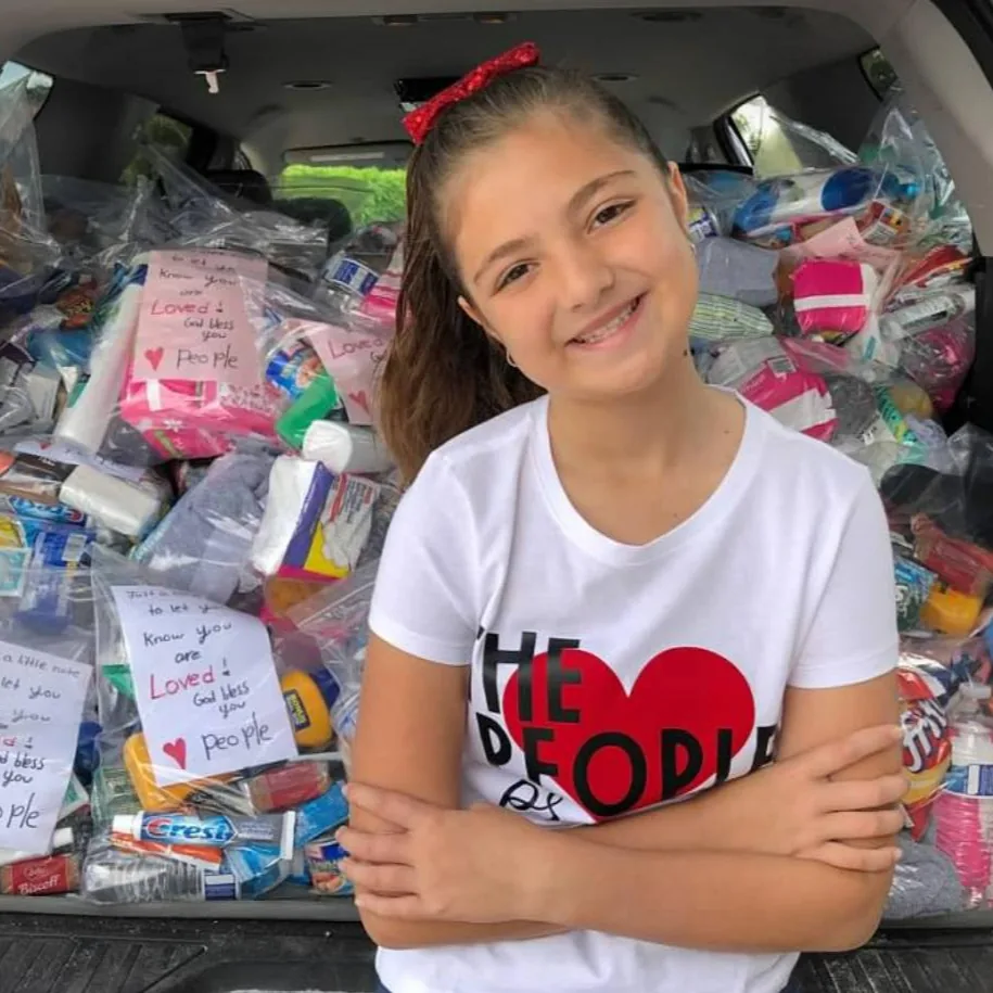 A young volunteer in front of a vehicle loaded with care packages