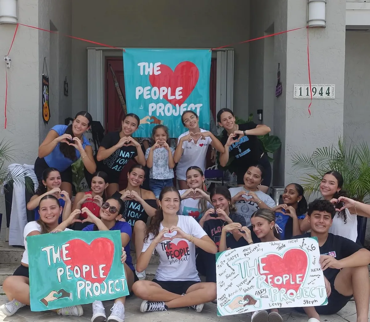 Youth volunteers making heart shapes with their hands behind Love People Project banners